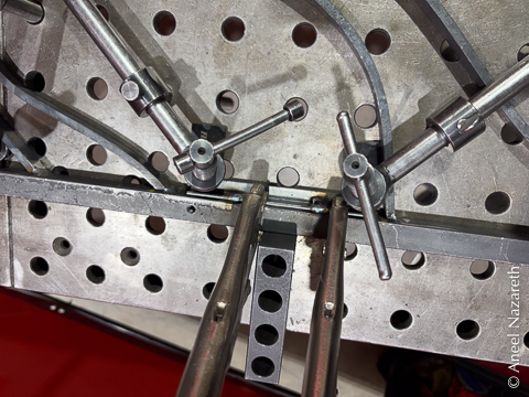 Clamps hold a small piece of angle iron down, while vise grips clamp it sideways to the frame